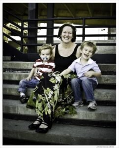 A smiling woman and two young boys sitting on concrete steps in an urban area.